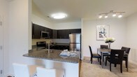 Located at 1150 Helen Drive in Newark, Delaware, this single-floor residence offers a thoughtfully designed living environment with modern finishes and an open, airy layout. The kitchen is a standout feature, showcasing rich dark cabinetry that extends to the ceiling, providing ample storage alongside a sleek granite countertop with bold veining. A peninsula with bar seating serves as both a functional workspace and a casual dining spot, seamlessly connecting the kitchen to the rest of the living area. Stainless steel appliances, including a refrigerator, microwave, and range, lend a contemporary, polished look to the space. The kitchen flows naturally into a dedicated dining area, which comfortably accommodates a full dining table and chairs, making it well-suited for both everyday meals and entertaining. Neutral-toned flooring and walls throughout create a bright, welcoming ambiance, complemented by recessed and flush-mount lighting that ensures the space is well-lit. The overall design balances practicality with style, offering a cohesive and functional living environment ideal for modern living.