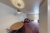 Located at 121 E Hoover Ave in Ann Arbor, Michigan, this one-bedroom, one-bathroom unit offers a practical and straightforward layout across a single floor. The combined living and dining area serves as the heart of the unit, featuring deep burgundy carpeting throughout and neutral white walls. A pendant light fixture hangs above the dining space, while the living area benefits from a large sliding glass door that draws in natural light and provides outdoor views. The bedroom is a comfortable size, featuring the same plush carpeting, a sliding closet, and its own window with access to outdoor light. Wood-paneled accent walls in portions of the space add a warm, retro character. Three closets throughout the unit provide generous storage options. The kitchen is tucked efficiently within the floor plan. The full bathroom features a tub/shower combination with floor-to-ceiling mosaic tile surround in earthy brown tones, a built-in wall niche, and a vanity with sink. The unit's layout is compact and functional, making efficient use of its footprint, and is situated within proximity to the University of Michigan campus and the amenities of downtown Ann Arbor.
