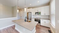 Located at 1980 Icon Way in Knoxville, Tennessee, this two-story home offers a well-planned layout across two levels. The ground floor houses a spacious attached garage equipped with an automatic opener, providing secure parking and interior access via a clean white panel door. A patterned-carpet staircase leads to the main living level above, where the majority of the home's space is found. The kitchen is a standout feature, showcasing white shaker-style cabinetry, a subway tile backsplash, stainless steel appliances, quartz countertops, and a large center island with an undermount sink and pendant lighting — all bathed in natural light from nearby windows. The open living area flows naturally from the kitchen, featuring light hardwood-style flooring, recessed lighting, a ceiling fan, and a tray ceiling detail. The bedroom is generously sized with a ceiling fan, hardwood-style floors, and a window overlooking lush, wooded surroundings. A dedicated closet provides ample storage. The full bathroom includes a tiled tub-shower combo with matte black fixtures, a window for natural light, and wood-look flooring. Outdoors, the property backs up to a natural, tree-lined hillside, offering a private and serene setting.