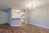 This single-floor residence offers a thoughtfully designed layout that balances comfort and functionality. The spacious living area welcomes you with rich wood-look flooring, neutral-toned walls, a textured ceiling, and a door providing direct outdoor access alongside a large window that fills the room with natural light. The living space flows seamlessly into a dining area, distinguished by an elegant chandelier, which connects directly to the kitchen via a half-wall breakfast bar. The galley-style kitchen is well-equipped with white cabinetry featuring warm wood trim accents, a gas range, a refrigerator, a dishwasher, and a double-basin sink — all finished with light wood-look flooring. The bedrooms are carpeted for comfort, with generous window arrangements that offer pleasant views of lush greenery. One bathroom features a clean, minimalist design with a tub and shower combination, while the second bathroom includes a vanity with cabinet storage, a mirror, and a built-in shelving unit for added organization. Throughout the home, consistent use of neutral tones, white trim, and wood-look flooring creates a cohesive, move-in-ready aesthetic that is both practical and inviting.
