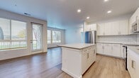 This well-appointed single-floor residence offers a clean, modern aesthetic with a thoughtfully designed open-concept layout. The kitchen serves as the centerpiece of the living space, featuring crisp white shaker cabinetry extending to the ceiling, a classic subway tile backsplash, a full suite of stainless steel appliances, and a spacious central island with a neutral-toned countertop that provides ample prep space and seating. Light wood-style flooring flows seamlessly throughout the home, complementing the bright white walls and recessed lighting overhead. The adjacent living area benefits from generous natural light, courtesy of large windows and a glass-panel door that opens to the outdoors, framing views of surrounding greenery. The bedrooms are well-proportioned with large windows fitted with horizontal blinds, and at least one bedroom includes a walk-in closet alongside a private en suite bathroom. The primary bathroom is outfitted with a dual-sink vanity, neutral quartz countertops, modern brushed nickel hardware, and a full soaking tub with white subway tile surround. A secondary bathroom offers a similarly refined single-vanity design. The overall ambiance is fresh, light, and move-in ready, reflecting a consistently modern and cohesive design sensibility throughout.