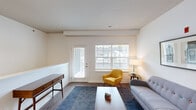 This single-floor residence offers a thoughtfully designed layout that balances comfort and functionality. The living room serves as a welcoming focal point, featuring rich hardwood-style flooring, a half-wall detail with chair rail molding, and abundant natural light streaming through a large window and a glass-panel exterior door that frames views of the surrounding neighborhood. The space flows into a dedicated dining area, which connects seamlessly to the kitchen. The kitchen is well-equipped with warm honey-toned cabinetry, granite countertops, stainless steel appliances including a refrigerator, range, and microwave, and a dark-toned island for additional prep space. The bedroom is carpeted for comfort and features a generously sized window with neighborhood views, providing a calm and restful atmosphere. An additional carpeted room offers flexible use as a home office or secondary bedroom. The bathroom is finished with a granite-topped vanity, warm wood cabinetry, and hardwood-style flooring, maintaining a cohesive aesthetic throughout. A dedicated in-unit laundry area with a full-size washer and dryer adds everyday convenience. Neutral white walls and consistent flooring choices create a clean, cohesive ambiance across all areas of the home.