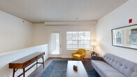 This single-floor residence offers a thoughtfully designed layout that balances comfort and functionality. The living room serves as a welcoming focal point, featuring rich hardwood-style flooring, a half-wall detail with chair rail molding, and abundant natural light streaming through a large window and a glass-panel exterior door that frames views of the surrounding neighborhood. The space flows into a dedicated dining area, which connects seamlessly to the kitchen. The kitchen is well-equipped with warm honey-toned cabinetry, granite countertops, stainless steel appliances including a refrigerator, range, and microwave, and a dark-toned island for additional prep space. The bedroom is carpeted for comfort and features a generously sized window with neighborhood views, providing a calm and restful atmosphere. An additional carpeted room offers flexible use as a home office or secondary bedroom. The bathroom is finished with a granite-topped vanity, warm wood cabinetry, and hardwood-style flooring, maintaining a cohesive aesthetic throughout. A dedicated in-unit laundry area with a full-size washer and dryer adds everyday convenience. Neutral white walls and consistent flooring choices create a clean, cohesive ambiance across all areas of the home.