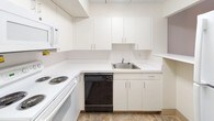 This single-floor, one-bedroom, one-bathroom unit offers a straightforward and functional layout designed for comfortable everyday living. The flooring throughout the unit features a stone-look tile pattern, providing a cohesive and easy-to-maintain surface across all rooms.

The kitchen is outfitted with white cabinetry extending to the ceiling, offering ample storage space. White laminate countertops run along an L-shaped configuration, accommodating a stainless steel sink, an electric coil range, a built-in microwave, and a black dishwasher. A pass-through window connects the kitchen to the adjacent living area, enhancing the sense of openness between spaces.

The living area is generously sized and receives natural light through a large window fitted with vertical blinds. Neutral beige walls and a paneled ceiling contribute to the room's clean, understated aesthetic.

The bedroom features a wide closet with a double rod system, providing practical storage. A doorway connects directly to the rest of the unit.

The bathroom includes a white vanity with cabinet storage and drawers, a mirrored medicine cabinet with overhead lighting, and a full-size tub and shower combination with white tile surround and chrome fixtures. The overall palette remains light and neutral throughout the unit.