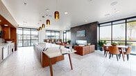 Located in Nashville, TN, this elegantly designed communal amenity space offers a seamless blend of modern aesthetics and functional design across a single open-plan floor. The interior is anchored by a striking gourmet kitchen, outfitted with warm wood cabinetry, a textured tile backsplash, stainless steel appliances, and a dramatic waterfall-edge stone island finished in bold white-and-charcoal veining. Amber-toned pendant lights hang overhead, casting a warm glow across the marble-look tile flooring that extends throughout the entire interior. Adjacent to the kitchen, a bar-height seating area with leather counter stools provides a casual gathering spot. The lounge area is defined by a bold dark feature wall hosting a linear fireplace and mounted display screen, flanked by plush leather sofas and lush potted greenery. Floor-to-ceiling black-framed windows wrap the perimeter, flooding the space with abundant natural light and framing sweeping views of the Nashville skyline. A dining area with leather chairs connects seamlessly to the lounge. Sliding glass doors open directly onto an expansive rooftop terrace, where raised garden planters with mature trees, wood-trimmed benches, and comfortable outdoor seating arrangements offer an inviting open-air retreat with unobstructed city and treetop views.