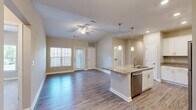 Located at 6452 Waymore Ln in Chester, VA, this single-floor, two-bedroom, two-bathroom home offers a well-designed layout that maximizes its comfortable footprint. The open-concept living and kitchen area serves as the heart of the home, characterized by vaulted ceilings that lend a sense of spaciousness and a ceiling fan overhead. Durable hardwood-style flooring runs throughout the main living spaces, complementing the neutral, warm-toned walls.

The kitchen features a central island with granite countertops, a built-in sink, and stainless steel appliances including a dishwasher, range, and microwave. White shaker-style cabinetry with brushed nickel hardware provides ample storage. Pendant lighting above the island adds a refined touch. Large windows in the living area allow natural light to fill the space, with a glass-panel entry door enhancing the bright, airy ambiance.

Both bedrooms are carpeted and include ceiling fans and closets. The generously sized primary bedroom connects to a well-appointed bathroom. The bathrooms feature granite-top vanities, hardwood-style flooring, and tub-shower combinations with brushed nickel fixtures. A dedicated laundry room houses a full-size Whirlpool washer and dryer, completing this functional and attractive home.