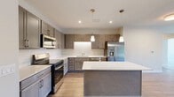 Located at 2805 Burton Rd in Ann Arbor, Michigan, this well-appointed 3-bedroom, 3-bathroom unit offers a thoughtfully designed single-floor layout. The open-concept kitchen and living area serves as the heart of the home, featuring warm hardwood-style flooring, taupe cabinetry, white quartz countertops, stainless steel appliances including a French door refrigerator, and a central island with pendant lighting above. The living area extends to a private balcony through sliding glass doors, offering outdoor views of the surrounding community.

Each of the three bedrooms is carpeted for comfort, with large windows that invite generous natural light and views of the greenery and community grounds. The primary bedroom is a comfortable retreat with its own dedicated bathroom. The bathrooms are finished with wood-look vinyl flooring, vanities with ample storage, and clean, neutral tones. One bathroom features a glass-enclosed walk-in shower, while another includes an accessible layout with grab bars. Two hallways connect the spaces efficiently, and a closet provides additional storage. The consistent use of soft, neutral tones throughout creates a calm, cohesive ambiance well-suited for everyday living.