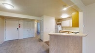 Located at 2216 E Cork St in Kalamazoo, Michigan, this single-floor residence offers a straightforward, functional layout with clearly defined living, kitchen, and sleeping areas. The open-concept living and dining space is carpeted in a neutral gray tone and benefits from generous natural light, courtesy of a sliding glass door that opens to an outdoor view of a grassy landscape — a standout feature that adds brightness and a sense of connection to the outdoors.

The kitchen is efficiently arranged in an L-shaped configuration, featuring white cabinetry with warm wood-tone trim, ample upper and lower storage, light countertops, and wood-look vinyl flooring. White appliances — including a gas range, refrigerator, and dishwasher — are included. A peninsula counter separates the kitchen from the living area, creating a natural transition between spaces.

The bedroom offers carpeted flooring and a window fitted with horizontal blinds, allowing adjustable natural light. A set of louvered bifold closet doors provides practical storage. The bathroom includes a wide vanity with a white countertop, wood-toned cabinetry below, a large mirror, and a shower/tub combination. Overall, the space presents a clean, neutral palette throughout.