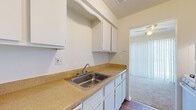 This two-floor residence is designed with a practical and clean aesthetic throughout. The main level features a carpeted living area with a large window fitted with vertical blinds, allowing ample natural light to fill the space. A front entry door provides direct access to this open area, which flows seamlessly toward the kitchen. The kitchen is laid out in a galley style, featuring white cabinetry, tan laminate countertops, a stainless steel sink, and wood-look flooring. White appliances, including a refrigerator and range, are included. A doorway from the kitchen leads to a staircase connecting the two floors. A half bathroom on the lower level includes tile flooring, a vanity with storage, and a toilet. Upstairs, the vaulted ceilings create a notably airy feel in the main upper living space, which is carpeted and bathed in light. The bedrooms are carpeted and equipped with ceiling fans and windows with outdoor views. A second full bathroom upstairs features wood-look flooring, a built-in shelving niche, a bathtub, and a toilet, rounding out the upper level's functional design.