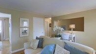 This two-floor residence offers a harmonious blend of comfort and refined style. The living area sets a welcoming tone with warm sandy-beige walls that provide a neutral backdrop for tasteful furnishings, including a plush cream sofa accented with soft blue and script-print throw pillows. Hardwood flooring anchors the space, adding warmth and a sense of continuity throughout.

Decorative touches elevate the ambiance — a pair of framed nature-inspired prints adorn one wall, while a sleek console table displays a graceful white orchid arrangement and a classic table lamp, adding an element of sophistication. A large mirror on the adjoining wall enhances the sense of depth and reflects natural light into the room.

The layout provides a clear sense of flow between spaces, with crisp white interior doors and clean trim work offering a polished contrast to the warmer wall tones. The neutral color palette throughout creates a calm, cohesive aesthetic that feels both livable and elegant.

Spanning two floors, this residence provides ample room for comfortable living, with each level contributing distinct functionality and character. The overall atmosphere is bright, serene, and thoughtfully curated, making it an inviting space suited for both relaxed everyday living and stylish entertaining.