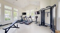 Located at 260 Lazelle Rd. in Columbus, OH, this dedicated fitness center offers a bright, modern workout environment designed to support a full range of exercise routines. The space features soaring vaulted ceilings that enhance the sense of openness, while an abundance of large windows along multiple walls floods the room with natural light and provides views of the surrounding greenery and outdoor pool area.

The gym is thoughtfully equipped with cardio machines including treadmills, an elliptical, and a stationary bike, complemented by a multi-function cable machine, a rowing machine, a full dumbbell rack, and an adjustable weight bench. Wall-mounted flat-screen televisions are positioned throughout for entertainment during workouts. A full-length mirror along one wall supports strength training and form checks.

The interior finishes are clean and minimalist, with neutral white walls and a light-colored durable floor surface that keeps the space feeling fresh and spacious. A wooden bench provides a convenient rest area, and a water fountain station near the entrance ensures easy hydration. French doors with glass panels lead to an adjacent area, completing the functional layout of this well-appointed community fitness center.