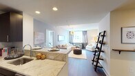 This thoughtfully designed single-floor residence offers a seamless blend of modern finishes and comfortable living across its well-proportioned layout. The open-concept living and dining area is anchored by rich hardwood flooring and a striking gold sputnik chandelier, with large windows framing impressive city skyline views and filling the space with natural light. A granite-topped kitchen island with an integrated sink transitions smoothly into the kitchen, which is outfitted with dark espresso cabinetry, stainless steel appliances including a refrigerator, electric range, and built-in microwave, providing a highly functional cooking space. The primary bedroom is generously sized, featuring wide windows with floor-to-ceiling draping that capture urban views, hardwood floors, and a serene, neutral palette. A second bedroom mirrors this calm aesthetic with soft tones and ample closet space. The primary bathroom showcases a sleek glass-enclosed walk-in shower with white tile and a stone-topped vanity, while the second bathroom offers a tub-shower combination with clean, classic tiling. Throughout the residence, soft neutral walls, recessed lighting, and cohesive dark wood flooring create a polished and inviting atmosphere suited to contemporary urban living.