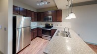 This single-floor residence at 435 Langtree Rd in Mooresville, NC offers a thoughtfully designed layout that balances functionality with comfort. The open-concept living and kitchen area serves as the heart of the home, featuring rich hardwood-style flooring, crown molding with sage green accents, and ceiling fans with integrated lighting. Track lighting illuminates the kitchen, which is equipped with dark espresso cabinetry, granite-style countertops, a tile backsplash, stainless steel appliances including a refrigerator, range, and microwave, and a peninsula with pendant lighting and a double-basin sink. A built-in bench nook provides a convenient transitional space between the main living area and the private quarters. Bedrooms are finished with plush carpet and feature ceiling fans, generous natural light, and sliding glass door access to an outdoor balcony in at least one room, offering pleasant exterior views. Bathrooms are well-appointed, with one featuring a soaking tub and a separate tile-surround shower with a glass enclosure, and another offering a dark wood vanity with a granite-style countertop and framed mirror. A dedicated laundry room with full-size washer and dryer hookups and overhead wire shelving adds further convenience to this well-rounded space.