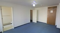 This single-floor space presents a straightforward and functional layout with a clean, neutral aesthetic throughout. The room visible in the space features smooth white walls and blue-grey carpeted flooring, creating a calm and understated atmosphere. A ceiling fan with a light fixture is centrally mounted, providing both ventilation and overhead lighting to the room. Dark baseboards offer a subtle contrast against the white walls and complement the carpeted floor. A doorway leads to a closet, providing convenient built-in storage and adding to the room's practicality. The open door reveals a carpeted closet interior, suggesting ample room for organization. The overall design is minimal and versatile, making the space well-suited for a variety of uses. The white walls reflect light effectively, keeping the interior feeling bright and open. The space is move-in ready in its current condition, with all essential elements in place for comfortable everyday use. Its clean lines and neutral palette provide a blank canvas that can easily be personalized to suit individual preferences and needs.