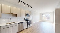 Located at 2211 S Grand Blvd in St. Louis, Missouri, this single-floor unit showcases a clean, contemporary design with a cohesive palette of light tones and modern materials throughout. The open-concept layout connects the kitchen and living area seamlessly, creating a bright and functional living environment.

The kitchen is a standout feature, equipped with full stainless steel appliances including a French door refrigerator, electric range, built-in microwave, and dishwasher. Light wood-grain cabinetry extends from floor to ceiling, complemented by a white penny-tile backsplash and light quartz countertops. Track lighting overhead adds a modern, directional illumination to the space. Light hardwood-style flooring runs throughout the main living areas, enhancing the sense of openness.

The bedrooms feature plush carpet flooring and are filled with natural light through large windows. One bedroom provides direct access to a private balcony through a glass-panel door, offering outdoor views of the surrounding neighborhood. A ceiling fan adds comfort to this room.

Two bathrooms serve the unit — one featuring a full tub-shower combination with white subway tile surround, and the other a vanity with storage cabinetry and hardwood-style flooring. A smart thermostat is also present, reflecting the unit's modern conveniences throughout.