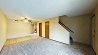 This two-floor residential space offers a practical and functional layout designed for comfortable everyday living. The main level features a spacious carpeted living area that provides a warm and inviting atmosphere. A ceiling fan with a light fixture is centrally positioned to ensure good air circulation and ambient lighting throughout the room. The living area is complemented by neutral-toned walls and classic wood-finished interior doors, lending a traditional aesthetic to the space. Tile flooring is visible in an adjacent area, offering a transition between living and utility zones. Multiple interior doors on the main level suggest additional rooms or storage areas nearby, adding to the overall functionality of the floor plan. A staircase with a dark wood handrail and white balustrade leads to the second floor, serving as a prominent architectural feature of the main level. The textured ceiling throughout adds a classic residential character. The overall design reflects a straightforward and well-organized layout, making efficient use of available space across both floors. This home is well-suited for those seeking a comfortable, multi-level living environment with traditional finishes and thoughtful spatial arrangement.
