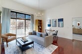 This thoughtfully designed 2-bedroom, 2-bathroom residence offers a seamless blend of modern style and functional living across a single floor. The living room immediately impresses with soaring ceilings, rich hardwood flooring, and floor-to-ceiling sliding glass doors that flood the space with natural light and open onto a private balcony overlooking lush, wooded surroundings. A contemporary chandelier adds an elegant focal point overhead.

The kitchen is a standout feature, showcasing warm cherry wood cabinetry, granite countertops, a slate tile backsplash, and a full suite of stainless steel appliances including a refrigerator, range, microwave, and dishwasher. A generous island provides additional prep and serving space, with a pass-through view connecting to the living area.

A gallery-style hallway lined with framed artwork leads to the private quarters. The primary bedroom is spacious and bright, with plush carpeting and multiple windows framing natural greenery. The second bedroom mirrors this comfort with its own large window and soft carpeted flooring. Both bathrooms are finished with tile flooring, granite-topped vanities, and warm wood cabinetry. A dedicated closet and hallway complete this well-organized layout.