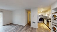 This single-floor unit offers a clean, functional layout designed for comfortable everyday living. The open-concept living and dining area is finished with light wood-tone laminate flooring that extends throughout the main living spaces, creating a bright and cohesive feel. Large windows allow natural light to filter in, enhancing the airy, neutral-toned interior defined by crisp white walls and white baseboards.

The kitchen is positioned adjacent to the living area and features stainless steel appliances, including a refrigerator and an electric range with an overhead ventilation hood. White cabinetry with brushed nickel hardware lines the walls, complemented by sleek gray countertops that provide ample prep space. A built-in floor vent ensures efficient climate control throughout the unit.

The bedrooms are carpeted for comfort and each includes a ceiling fan with a light fixture, as well as windows with vertical blinds that offer views of surrounding greenery. The layout connects seamlessly through a central hallway leading to additional rooms and closet storage.

The bathroom is finished with light wood-tone flooring and features a white vanity with brushed nickel fixtures, a large mirror with overhead lighting, and a full tub-shower combination. Clean white walls and coordinated hardware give the bathroom a polished, practical look throughout.