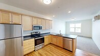 Located on the third floor at 268 E Allen St in Winooski, Vermont, Unit 304 is a thoughtfully laid-out one-bedroom, one-bathroom residence that makes efficient use of its space. The open-concept kitchen and living area serves as the heart of the unit, featuring light maple cabinetry, dark countertops, and a full suite of stainless steel appliances including a refrigerator, electric range, built-in microwave, and dishwasher. Warm hardwood flooring runs throughout the kitchen, entry hallway, and common areas, lending a bright, cohesive feel to the space. Natural light filters in through windows in the living area, enhancing the clean, neutral palette of white walls and light finishes throughout. The entry hallway is well-organized, with coat hooks and access to both the bathroom and bedroom. The spacious bedroom features plush carpeting, a large window with outdoor views, a baseboard heater, and a double-door closet offering generous storage. The full bathroom includes a tub-shower combination with a curtain rod, toilet, and hardwood-style flooring. The unit's simple, modern aesthetic and practical layout make it a comfortable and functional home in the heart of Winooski.