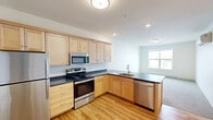 Located on the third floor at 268 E Allen St in Winooski, Vermont, Unit 304 is a thoughtfully laid-out one-bedroom, one-bathroom residence that makes efficient use of its space. The open-concept kitchen and living area serves as the heart of the unit, featuring light maple cabinetry, dark countertops, and a full suite of stainless steel appliances including a refrigerator, electric range, built-in microwave, and dishwasher. Warm hardwood flooring runs throughout the kitchen, entry hallway, and common areas, lending a bright, cohesive feel to the space. Natural light filters in through windows in the living area, enhancing the clean, neutral palette of white walls and light finishes throughout. The entry hallway is well-organized, with coat hooks and access to both the bathroom and bedroom. The spacious bedroom features plush carpeting, a large window with outdoor views, a baseboard heater, and a double-door closet offering generous storage. The full bathroom includes a tub-shower combination with a curtain rod, toilet, and hardwood-style flooring. The unit's simple, modern aesthetic and practical layout make it a comfortable and functional home in the heart of Winooski.