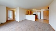 This single-floor unit offers a practical and comfortable layout designed for everyday living. The open-concept living area is carpeted and filled with natural light, thanks to a large sliding glass door that leads to an outdoor patio area. A baseboard heating system runs along the walls, ensuring consistent warmth throughout the space.

The kitchen is efficiently designed with warm oak cabinetry — both upper and lower — providing generous storage and counter space. It is equipped with a full suite of white appliances, including a refrigerator, electric range, and over-the-range microwave. A peninsula-style breakfast bar separates the kitchen from the living area, creating a natural flow between the two spaces. Tile flooring runs throughout the kitchen, contrasting with the soft carpet of the adjoining living areas.

The bedrooms are carpeted and well-lit by windows with vertical blinds. One bedroom features a ceiling fan with integrated lighting and a sliding-door closet, offering practical storage. The second bedroom is a quiet, naturally lit space with a baseboard heater.

The bathroom is clean and functional, featuring a full soaking tub and shower combination with safety grab bars, tile flooring, and warm wood-toned doors that complement the overall aesthetic of the unit. The layout throughout is straightforward and move-in ready.