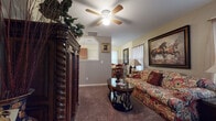 Located at 5323 East Harry Street in Wichita, Kansas, this single-story home offers a welcoming and well-appointed interior with a cohesive, warm aesthetic throughout. The living room serves as the heart of the home, featuring plush carpeting, a ceiling fan with light fixture, and ample natural light filtering through curtained windows. A richly detailed dark wood armoire anchors one side of the room, while a patterned sofa and loveseat arrangement, complemented by an oval coffee table, creates a comfortable and inviting seating area. Decorative framed artwork, including a striking equestrian painting, adds character to the walls. The kitchen is efficiently laid out with warm wood cabinetry, granite-look countertops, a tiled backsplash, and light tile flooring. It includes a dishwasher, refrigerator, and a double sink beneath upper cabinets, with convenient access to an exterior door. The dining area is an intimate space bathed in natural light from a sheer-curtained window, centered around a round wood table with classic wood chairs. The bedroom offers a quiet retreat with a window dressed in deep burgundy curtains and tasteful wall art. The home's single-floor layout ensures easy accessibility and a cohesive flow between all living spaces.