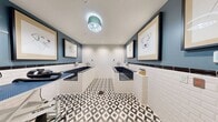 This 130 square foot space in Bethesda, MD, is a well-designed pet grooming facility that combines functionality with aesthetic appeal. The room is dominated by crisp white subway tiles that line the walls, creating a clean and hygienic environment. A striking geometric black and white patterned floor adds visual interest and complements the overall design.

The space features multiple grooming stations, including raised bathing tubs with chrome fixtures and adjustable grooming tables. A sleek blue accent wall provides a pop of color and serves as a backdrop for three framed dog portraits, adding a touch of whimsy to the professional setting.

Large glass doors or windows allow natural light to flood the space, enhancing visibility and creating an open feel. The room is equipped with modern amenities such as wall-mounted hairdryers and easily accessible power outlets. Storage solutions are seamlessly integrated into the design, maintaining the space's clean lines.

The combination of durable materials, efficient layout, and thoughtful design elements creates a space that is both practical for pet grooming services and visually appealing to pet owners. The attention to detail in this compact yet well-appointed facility demonstrates a commitment to providing a high-quality grooming experience.