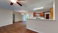 This single-floor residence offers three bedrooms and two bathrooms within a practical, well-organized layout. The open-concept living and dining area is anchored by rich hardwood-style flooring and a ceiling fan with light fixture, creating a comfortable and airy atmosphere. A chandelier over the dining space adds a decorative touch, while a sliding glass door allows natural light to filter into the main living area.

The kitchen is outfitted with warm-toned wood cabinetry, white countertops, and stainless steel appliances including an electric range and refrigerator. A peninsula-style counter divides the kitchen from the living space, providing additional prep and serving area. Hardwood-style flooring continues throughout the kitchen for a cohesive look.

Each of the three bedrooms features neutral-toned carpet, textured ceilings, and windows with blinds that bring in natural light. The rooms offer ample open floor space suitable for various furnishing arrangements. Both bathrooms include wood-toned vanity cabinetry, white countertops, and hardwood-style flooring. One bathroom features a full tub-shower combination with floor-to-ceiling tile surround and a large vanity mirror with overhead lighting.