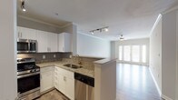 This single-floor residence offers a thoughtfully designed open-concept layout that seamlessly connects the kitchen and living area. The kitchen is a standout feature, equipped with stainless steel appliances including a gas range, over-the-range microwave, and dishwasher. White shaker-style cabinetry, granite countertops, a subway tile backsplash, and a peninsula with a stainless steel sink complete the space with a clean, modern aesthetic. Track lighting above the kitchen and peninsula adds functional illumination throughout.

The living area is generously proportioned, featuring wood-look laminate flooring, crown molding, and a ceiling fan. French doors along the far wall flood the space with natural light and provide outdoor access, enhancing the open and airy atmosphere.

The bedrooms are carpeted for comfort, each offering ceiling fans and windows with natural light. The neutral tones and clean lines throughout lend a calm, move-in-ready ambiance.

The bathroom is finished consistently with the kitchen, featuring a white vanity with granite countertops, a framed mirror, overhead lighting, and wood-look flooring. Additional storage cabinetry above the toilet maximizes functionality. Overall, this residence presents a cohesive, contemporary design with quality finishes from room to room.