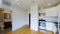 Musical String House is a thoughtfully designed single-floor residence that combines clean, modern aesthetics with functional living. The space is characterized by crisp white walls, recessed lighting, and warm-toned hardwood floors that run seamlessly throughout, creating a cohesive and inviting atmosphere.

The kitchen is a standout feature, outfitted with stainless steel appliances including a gas range, built-in microwave, and oven. White cabinetry with a classic shaker-style design reaches toward the ceiling, maximizing storage, while a tiled backsplash adds a subtle decorative element. Dark stone countertops provide a striking contrast to the light cabinetry, lending the kitchen a polished, contemporary feel.

The open layout connects the kitchen to the surrounding living areas, promoting a natural flow between spaces. Louvered closet doors add a practical storage element while maintaining the clean visual lines of the interior. Ample wall space offers flexibility for furniture arrangement and personalization.

Ceiling-mounted HVAC vents suggest a central climate control system, contributing to year-round comfort. The generous ceiling height enhances the sense of openness throughout the home. Overall, Musical String House presents a well-appointed, move-in-ready space with modern conveniences and a bright, airy character.