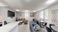 Located at 4545 Valley View Rd in Edina, MN, this party room is a well-appointed, single-floor communal space designed to accommodate a variety of gatherings and social events. The layout seamlessly integrates a fully equipped kitchen with an open living and dining area, making it both practical and inviting.

The kitchen is outfitted with white cabinetry, a full-size refrigerator, electric range, microwave, and a stainless steel sink. A long, light-toned countertop peninsula serves as both a workspace and a natural divider between the kitchen and the main gathering area, providing ample prep and serving space. Pendant lighting overhead adds a functional, clean aesthetic.

The living area features patterned carpeting and neutral gray walls that create a calm, flexible backdrop. A sectional leather sofa, a marble-top coffee table, and a wall-mounted flat-screen TV offer comfortable lounging options, while multiple round tables and chairs accommodate seated dining or group activities. Additional folding chairs are stored on-site for expanded seating. Natural light filters in through window blinds, and flush-mount ceiling lights ensure the space is well-lit throughout. A wall-mounted HVAC unit provides climate control. The overall ambiance is clean, functional, and welcoming — well-suited for community events and private gatherings alike.