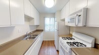This single-floor residence offers a thoughtfully laid-out interior highlighted by a striking living area with soaring vaulted ceilings and exposed white-painted wooden beams. Warm hardwood flooring runs throughout the main living spaces, complementing the abundance of natural light that filters in through large sliding glass doors opening to a private balcony overlooking lush greenery. The open sightlines and generous ceiling height create a sense of spaciousness and airiness rarely found in comparable residences. A clerestory window further enhances brightness in the living area, while a ceiling fan adds functional comfort.

The galley-style kitchen is efficiently designed with white cabinetry, earthy laminate countertops, a double stainless steel sink, and white appliances including a gas range, over-the-range microwave, and refrigerator. Hardwood flooring and a window with vertical blinds complete the kitchen's clean, practical aesthetic.

The bedrooms feature neutral carpet, textured ceilings, and mirrored sliding closet doors that maximize storage and reflect light. A wall-mounted HVAC unit ensures climate control. The bathroom is well-appointed with a tub and shower enclosed by sliding glass doors, a white vanity, and simple, clean finishes. Throughout, the space maintains a cohesive, neutral palette that feels bright and move-in ready.