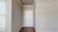This single-story, 2-bedroom, 2-bathroom residence offers a thoughtfully designed layout that balances comfort and functionality. The entryway greets visitors with rich dark hardwood-style flooring and elegant crown molding that carries throughout the main living areas, establishing a polished aesthetic from the moment you step inside.

The open-concept living room is generously sized, bathed in natural light through multiple windows fitted with blinds, and flows seamlessly into the kitchen. The kitchen is a standout feature, showcasing dark espresso cabinetry, a tile backsplash, stainless steel appliances including a microwave, range, and refrigerator, and a curved granite-topped island with pendant lighting above — an ideal space for both cooking and casual dining.

Both bedrooms are carpeted for comfort and include ceiling fans, natural light, and dedicated closets with wire shelving systems offering practical storage. The primary bedroom is a comfortable size with its own well-appointed bathroom. The bathrooms feature dark wood vanities with granite countertops, tile-surround tub-shower combinations, and dark hardwood-style flooring. A convenient hallway connects all areas of the home, and two closets provide additional storage throughout. The warm, neutral taupe color palette creates a cohesive and inviting atmosphere throughout the entire residence.