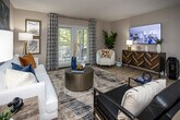 Located at 1000 Country Oak Cir in Knoxville, Tennessee, this thoughtfully designed single-floor residence offers a cohesive blend of modern style and comfortable living. The spacious living room serves as the heart of the home, featuring light wood-style flooring, a textured ceiling, and a striking blue accent wall adorned with bold abstract artwork. Natural light pours in through French doors dressed with patterned curtains, creating a bright and welcoming atmosphere. The open layout provides ample room for diverse seating arrangements and leads seamlessly to the outdoor area.

The kitchen is well-appointed with stainless steel appliances, including a range, over-the-range microwave, and refrigerator. White upper cabinetry pairs elegantly with gray lower cabinets, all complemented by granite-style countertops. A skylight adds an extra touch of natural brightness to the space.

The bedroom is a serene retreat, complete with plush carpeting, a ceiling fan, and soft neutral tones accented by a decorative striped feature wall. Large windows allow for natural light while maintaining privacy. The bathroom offers a tub-shower combination with tile surround and granite-topped vanity, rounding out this well-appointed Knoxville residence.