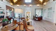 Located at 2905 Chastain Meadows Pkwy in Marietta, Georgia, this single-floor community space delivers a striking first impression through its sophisticated architectural design and warm, coastal-inspired aesthetic. The main area commands attention with soaring vaulted ceilings clad in rich wood paneling, exposed structural beams, and a combination of wide-plank hardwood and brick flooring that adds rustic charm. Dramatic exposed brick walls with arched passageways divide the open layout while maintaining a sense of flow and connectivity between zones.

The primary gathering area features a tufted leather sofa, layered area rugs, and a fireplace framed in brick — creating an inviting, lounge-like atmosphere. Adjacent to this is a dedicated workspace outfitted with dark wood desks topped in polished granite, rattan seating, and floral drapery panels that frame large windows flooding the space with natural light.

A quieter consultation room offers soft blue wainscoted walls, wall sconces, landscape artwork, and a glass-topped table — ideal for private meetings. A secondary sitting nook features wingback chairs, brick-tiled flooring, and generous windows overlooking the outdoors. Throughout, the cohesive use of teal and aqua accents, botanical drapery, and curated furnishings lends a refined yet approachable character to the entire space.