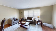 This two-story home offers a practical and well-organized layout spread across two floors. The main level features a combined kitchen and living room area, a hallway, a laundry room, and a full bathroom. The living room is bright and welcoming, with warm hardwood-style flooring, crown molding, and a large window fitted with wide-slat blinds that allow natural light to fill the space. The kitchen is equipped with white cabinetry, granite-style countertops, and full-size appliances, including a black refrigerator, with direct access to additional rooms via a connecting hallway.

The upper floor houses both bedrooms, a second hallway, and a second full bathroom. The generously sized primary bedroom features plush carpeting and ample room for furnishings. The second bedroom is comparably comfortable, also carpeted, with large windows that offer views of surrounding greenery. Both bathrooms are similarly appointed, each featuring wood-look vinyl flooring, white vanities with granite-style counters, and a tub-shower combination with a curtain enclosure. Neutral warm-beige tones are carried throughout the home, creating a cohesive and calm atmosphere. The staircase connects both levels efficiently, making the overall flow of the home straightforward and easy to navigate.