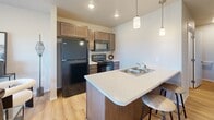 This three-story residence offers a thoughtfully organized layout across its floors, making efficient use of every level. The ground floor serves as a practical entry point, featuring a mudroom-style entrance with a built-in bench, wall-mounted coat hooks, and carpeted stairs leading upward — establishing a welcoming and organized transition into the home.

The main living floor hosts the heart of the residence: an open-concept kitchen and living room finished with warm hardwood-style flooring. The kitchen is equipped with stainless and black appliances, including a range, microwave, and refrigerator, complemented by shaker-style cabinetry and a light quartz peninsula with an integrated sink and pendant lighting above. The adjacent living area benefits from large windows that invite natural light and outdoor views, creating a bright, airy atmosphere. A half bath with vaulted ceiling detail is also accessible on this level.

The upper floor contains both bedrooms, each carpeted for comfort. The primary bedroom features a ceiling fan and connects to a hallway leading to the full bathroom, which includes a tub-shower combination, dark wood vanity, and neutral tile flooring. A second bedroom with a window overlooking the exterior rounds out the upper level, alongside closets and a connecting hallway.