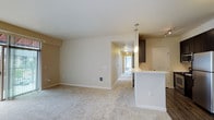 This single-floor residence offers a thoughtfully designed layout with a neutral, warm color palette throughout. The open-concept living and kitchen area forms the heart of the home, where plush wall-to-wall carpeting in the living space transitions to wood-look flooring in the kitchen. The kitchen is well-equipped with dark espresso cabinetry reaching toward the ceiling, stainless steel appliances including a refrigerator, range, and microwave, and a white peninsula counter that doubles as a breakfast bar. Pendant lighting above the peninsula adds a modern touch.

The living area connects to a private outdoor space via sliding glass doors, bringing in natural light. A hallway leads to the bedrooms, each finished with soft carpeting, baseboard heating, and generous windows fitted with vertical blinds that frame outdoor views. One bedroom features a ceiling fan and dual windows, while another benefits from corner window placement for added brightness.

The two bathrooms are finished consistently with dark vanity cabinetry, white countertops, and wood-look flooring. One bathroom includes a shower/tub combination, while the other features an adjacent linen closet. A spacious walk-in closet with wire shelving provides ample storage.