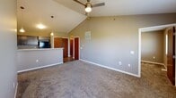 Located at 4131 W 54th St N in Sioux Falls, South Dakota, this single-floor home is designed with an open, functional layout and quality finishes throughout. The living area is a standout feature, showcasing soaring vaulted ceilings that lend a sense of spaciousness and airiness to the space. A ceiling fan complements the room, and large windows allow natural light to pour in, offering views of the surrounding neighborhood. A glass-paneled exterior door provides direct access to an outdoor area.

The kitchen is well-appointed with dark-toned cabinetry, light granite-style countertops offering generous prep space, and stainless hardware accents. Pendant lighting hangs above a kitchen peninsula that includes a sink, creating a natural divide between the kitchen and living areas. Dark hardwood-style flooring grounds the kitchen zone.

The bedrooms are carpeted and neutrally toned, each receiving natural light through windows with outdoor views. Closet storage is included in the bedrooms. The bathroom is finished with wood-look tile flooring, a dark vanity with a white countertop, a lighted mirror, and a full tub-shower combination. Neutral taupe walls and white trim carry consistently throughout, giving the home a cohesive, modern aesthetic.