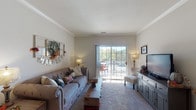 Located on White Magnolia Drive in O'Fallon, Missouri, this single-floor residence offers a well-organized layout designed for comfortable everyday living. Crown molding details are present throughout the main living areas, adding a refined architectural touch to the interior.

The living room serves as the central gathering space, featuring plush carpeting, generous natural light, and a large sliding glass door that opens to a private balcony with outdoor views of surrounding greenery. The open sightlines create an inviting and airy atmosphere.

The kitchen is positioned adjacent to the living area and features warm oak cabinetry, a double-basin stainless steel sink, a breakfast bar peninsula, and white appliances including a range, microwave, dishwasher, and refrigerator. Wood-style flooring grounds the space practically.

The primary bedroom is spacious and carpeted, with a window allowing natural light to filter in. It includes direct access to a private en-suite bathroom equipped with an oak vanity, a large mirror with overhead lighting, and a shower-tub combination with wood-style flooring.

A second bedroom offers comfortable proportions with carpet flooring and a window with views. A second full bathroom serves this area of the residence, also featuring wood-style flooring and a shower-tub combination.