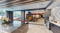 Located at 509 N Mangum St in Durham, NC, this single-floor commercial space presents a sophisticated and modern interior designed to accommodate a variety of uses. The lobby is anchored by polished marble-look tile flooring that flows seamlessly throughout, lending an air of refinement to the entire space. A striking dark veined marble countertop bar with red and gold-accented stools serves as a central feature, providing both a functional workspace and a social gathering point. Large floor-to-ceiling windows flood the interior with natural light and offer views of the surrounding streetscape, while patterned frosted glass panels add privacy without sacrificing brightness. Seating options are diverse and thoughtfully arranged: bold mustard yellow banquette booths with dark marble tables anchor one zone, while deep rust-red upholstered booth seating with white tabletops creates intimate nooks along another wall. A separate glass-enclosed room, accented by a vivid red-and-white chevron feature wall, provides a private meeting or lounge area. Decorative linear ceiling elements, pendant lighting, and a warm, eclectic mix of textures and colors — including teal, terracotta, and charcoal — give the space a dynamic yet welcoming ambiance suited for a modern professional environment.