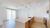 Located at 2490 N Druid Hills Rd in Atlanta, GA, this modern 1-bedroom, 2-bathroom residence offers a thoughtfully designed open-concept layout finished with light hardwood flooring and crisp white walls throughout. The combined kitchen and living area serves as the heart of the home, anchored by a sleek peninsula with white quartz countertops and an undermount stainless steel sink. Warm natural wood cabinetry pairs beautifully with a white subway tile backsplash, stainless steel appliances, and a trio of globe pendant lights that add a contemporary touch. Sliding glass doors in the living area lead to a private balcony, framing serene wooded views and allowing natural light to fill the space. The bedroom is comfortably sized, featuring a large window overlooking the tree canopy and access to the balcony. Both bathrooms are finished in a clean, modern style, each featuring glass-enclosed walk-in showers with large-format tile, wood-tone vanities, and white quartz countertops. A dedicated closet and in-unit laundry add to the home's practical functionality. Light, airy, and move-in ready, this residence combines modern design with a tranquil natural setting in the heart of Atlanta.