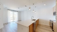 Located at 2490 N Druid Hills Rd in Atlanta, GA, this modern 1-bedroom, 2-bathroom residence offers a thoughtfully designed open-concept layout finished with light hardwood flooring and crisp white walls throughout. The combined kitchen and living area serves as the heart of the home, anchored by a sleek peninsula with white quartz countertops and an undermount stainless steel sink. Warm natural wood cabinetry pairs beautifully with a white subway tile backsplash, stainless steel appliances, and a trio of globe pendant lights that add a contemporary touch. Sliding glass doors in the living area lead to a private balcony, framing serene wooded views and allowing natural light to fill the space. The bedroom is comfortably sized, featuring a large window overlooking the tree canopy and access to the balcony. Both bathrooms are finished in a clean, modern style, each featuring glass-enclosed walk-in showers with large-format tile, wood-tone vanities, and white quartz countertops. A dedicated closet and in-unit laundry add to the home's practical functionality. Light, airy, and move-in ready, this residence combines modern design with a tranquil natural setting in the heart of Atlanta.