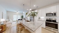 This single-floor residence offers a thoughtfully designed open-concept layout that seamlessly connects the kitchen, dining, and living areas. The kitchen serves as the centerpiece of the home, featuring a large granite-topped island with an undermount sink, pendant lighting, crisp white shaker cabinetry, subway tile backsplash, and a full suite of stainless steel appliances. Light hardwood flooring runs throughout the main living areas, complementing the bright, neutral color palette.

The living room is airy and welcoming, bathed in natural light through large French doors that open to the outdoors. A ceiling fan adds both function and style to the comfortable space. The bedrooms are serene retreats, finished with the same light hardwood floors and ceiling fans, offering a calm and restful atmosphere.

The bathroom is well-appointed with granite countertops, white cabinetry, a tub-shower combination, and access to a spacious walk-in closet with built-in shelving. Recessed lighting and large windows throughout ensure the home remains bright and inviting. The consistent use of clean whites, natural wood tones, and soft neutrals gives this residence a cohesive, modern aesthetic with a warm, livable character.
