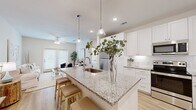 This single-floor residence offers a thoughtfully designed open-concept layout that seamlessly connects the kitchen, dining, and living areas. The kitchen serves as the centerpiece of the home, featuring a large granite-topped island with an undermount sink, pendant lighting, crisp white shaker cabinetry, subway tile backsplash, and a full suite of stainless steel appliances. Light hardwood flooring runs throughout the main living areas, complementing the bright, neutral color palette.

The living room is airy and welcoming, bathed in natural light through large French doors that open to the outdoors. A ceiling fan adds both function and style to the comfortable space. The bedrooms are serene retreats, finished with the same light hardwood floors and ceiling fans, offering a calm and restful atmosphere.

The bathroom is well-appointed with granite countertops, white cabinetry, a tub-shower combination, and access to a spacious walk-in closet with built-in shelving. Recessed lighting and large windows throughout ensure the home remains bright and inviting. The consistent use of clean whites, natural wood tones, and soft neutrals gives this residence a cohesive, modern aesthetic with a warm, livable character.