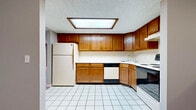 Located at 53 Oakridge Dr in Buffalo, NY, this single-floor residence offers a practical and straightforward layout designed for comfortable everyday living. The kitchen is well-equipped with warm oak cabinetry providing generous upper and lower storage, white tile flooring, a skylight panel for added brightness, a stainless steel sink, electric range with coil burners, dishwasher, and a full-size refrigerator — making it a fully functional cooking space. White countertops and a tile backsplash complete the clean, utilitarian aesthetic. The living areas feature rich hardwood flooring in a warm tone, complemented by neutral gray walls throughout. A large sliding glass door floods one of the main living spaces with natural light and provides direct access to an outdoor patio area with views of the surrounding greenery. A mirrored accent wall with a half-wall divider adds a sense of depth and openness to the entryway or dining area. The carpeted bedrooms offer a quieter, softer underfoot experience, each with windows that bring in natural light. Textured ceilings are present throughout the home. Overall, the space presents a clean, move-in ready environment in a residential Buffalo neighborhood.