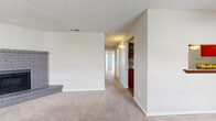 This well-organized single-floor residence features two bedrooms and two bathrooms within a practical and efficient layout. The combined living and dining area provides a welcoming entry point, highlighted by a classic brick fireplace and neutral-toned carpet throughout. A window at the front fills the space with natural light, creating a bright and comfortable atmosphere. The kitchen is thoughtfully designed with warm wood cabinetry, mosaic tile backsplash, granite-style countertops, and wood-look vinyl flooring. A charming pass-through window connects the kitchen to the dining area, enhancing the open feel of the shared living space. The primary bedroom is a comfortable retreat featuring plush carpeting, a ceiling fan, and a sliding glass door that opens to a private balcony with outdoor views. The second bedroom is similarly carpeted and well-proportioned, with easy access to the hallway. Both bathrooms are clean and functional, with one featuring a full tub-shower combination with white tile surround and wood cabinetry above. Two closets provide ample storage throughout the unit. A central hallway connects all rooms efficiently, completing the cohesive and practical floor plan of this inviting home.