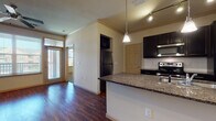 This single-floor residence is designed with a clean, functional layout that balances open communal spaces with private retreats. The kitchen serves as a central highlight, featuring dark espresso cabinetry, granite countertops, a subway tile backsplash, and stainless steel appliances including a refrigerator, range, and over-the-range microwave. A peninsula with an undermount sink and pendant lighting above creates a natural divide between the kitchen and the living area, while also offering additional prep and seating space.

The living area is open and generously proportioned, finished with rich hardwood-style flooring that extends throughout the main living spaces. Crown molding, track lighting, and a ceiling fan add to the polished feel of the room. Large windows with blinds allow abundant natural light to fill the space, and a door provides access to an outdoor balcony or patio area.

The bedroom is carpeted and features an arched window that frames an outdoor view, along with a ceiling fan for comfort. Adjacent to the bedroom is a full bathroom appointed with granite countertops, dark cabinetry, a large vanity mirror, and tile flooring. A separate tub and shower are also present, and a walk-in closet with built-in shelving provides ample storage. A smart thermostat is also installed for modern climate control.