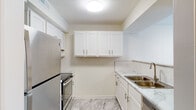 This single-floor unit offers a thoughtfully updated interior with a clean, neutral palette and consistent finishes throughout. The kitchen is a standout feature, showcasing crisp white shaker cabinetry, marble-style countertops, a white subway tile backsplash, and stainless steel appliances including an electric range and refrigerator. A double-basin sink and overhead range hood complete the functional layout.

The living areas are finished with warm-toned laminate wood flooring and feature ceiling fans with integrated lighting. One of the main living spaces includes a corner fireplace, adding a welcoming focal point to the room. Adjacent areas display classic wainscoting detailing, contributing to the unit's traditional character.

The bedrooms are bright and airy, with large windows allowing natural light to filter in, complemented by light wood-tone flooring and textured ceilings. Multiple six-panel doors connect the well-organized layout.

Two bathrooms serve the unit, each finished with marble-style countertops, white vanity cabinetry, brushed nickel hardware, and wood-look flooring. One bathroom includes a full shower-tub combo, while the other offers a convenient half-bath configuration. Together, the spaces present a cohesive, move-in ready interior with modern updates and comfortable proportions throughout.