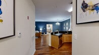 Located in Broadlands, VA, this well-appointed 2-bedroom, 2-bathroom residence offers a thoughtfully designed single-floor layout. The living room makes a strong first impression with rich hardwood flooring, crown molding, large windows that invite natural light, and a bold navy accent wall adorned with circular mirrors. The adjoining dining area continues the navy accent wall theme, complemented by a chandelier overhead and the same warm hardwood flooring throughout. The kitchen is equipped with stainless steel appliances, including a gas range, microwave, and refrigerator, set against dark granite countertops and light wood cabinetry. A peninsula provides additional prep space and opens to the main living areas. The spacious primary bedroom features plush carpet, a ceiling fan, large windows with full-length draping, and neutral gray tones for a serene retreat. The second bedroom offers a cozy atmosphere with a blue accent wall, carpet flooring, and ample natural light. Both bathrooms are clean and functional, with one featuring a full tub-shower combination with tiled surround. A dedicated laundry area houses a full-size washer and dryer. Two closets and two hallways provide generous storage throughout.